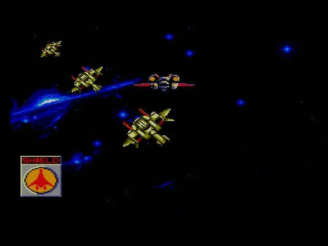 El caça de Galaxy Force vola per l’espai davant d’una formació enemiga, amb l’indicador SHIELD a l’esquerra.