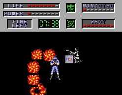 Joe Musashi envoltat per diverses explosions de foc mentre un enemic s'acosta.