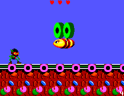 Zool combat un gran enemic volador verd i groc sobre una plataforma de dolços.
